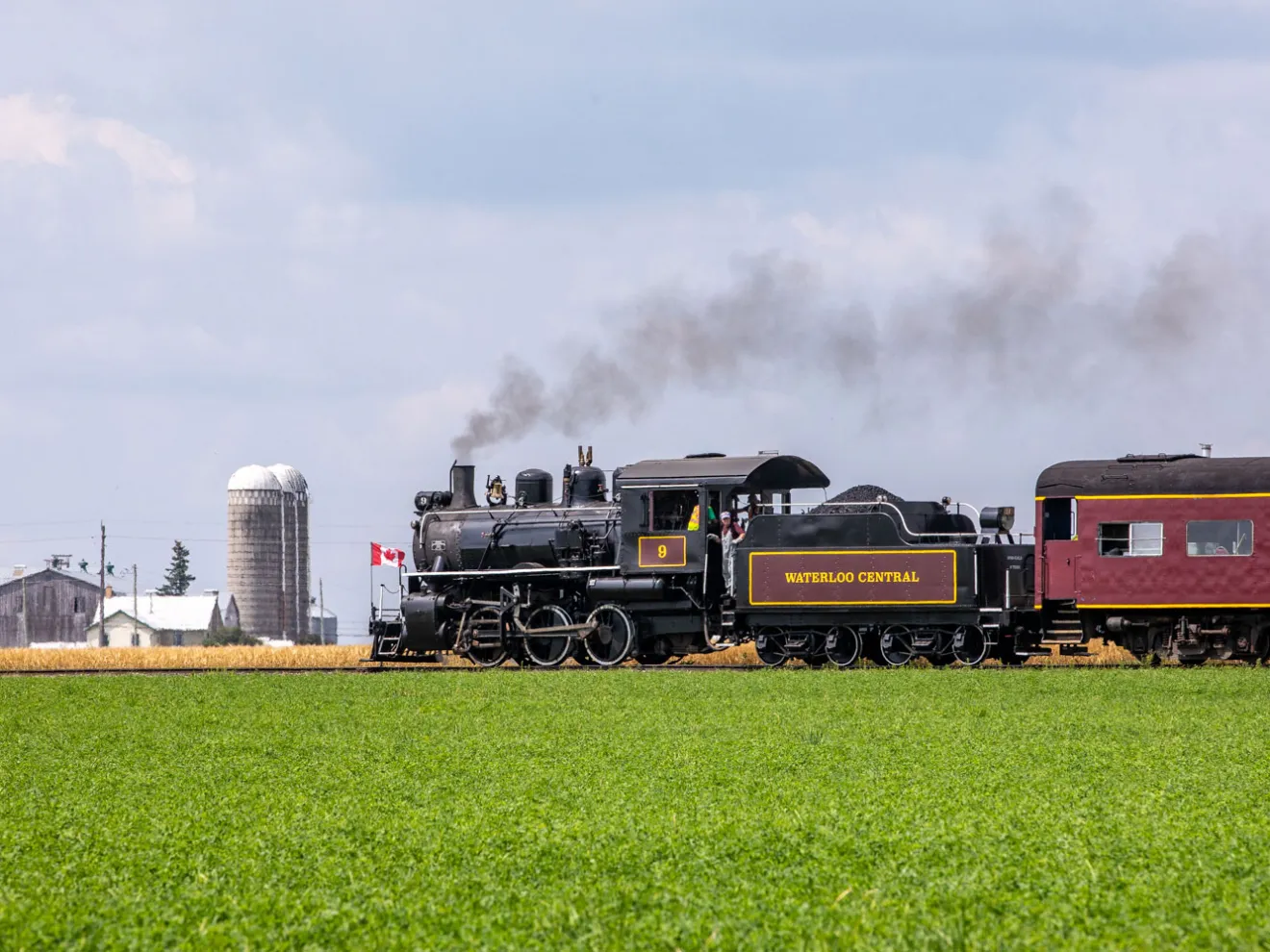 a steam engine train traveling down train tracks near a field