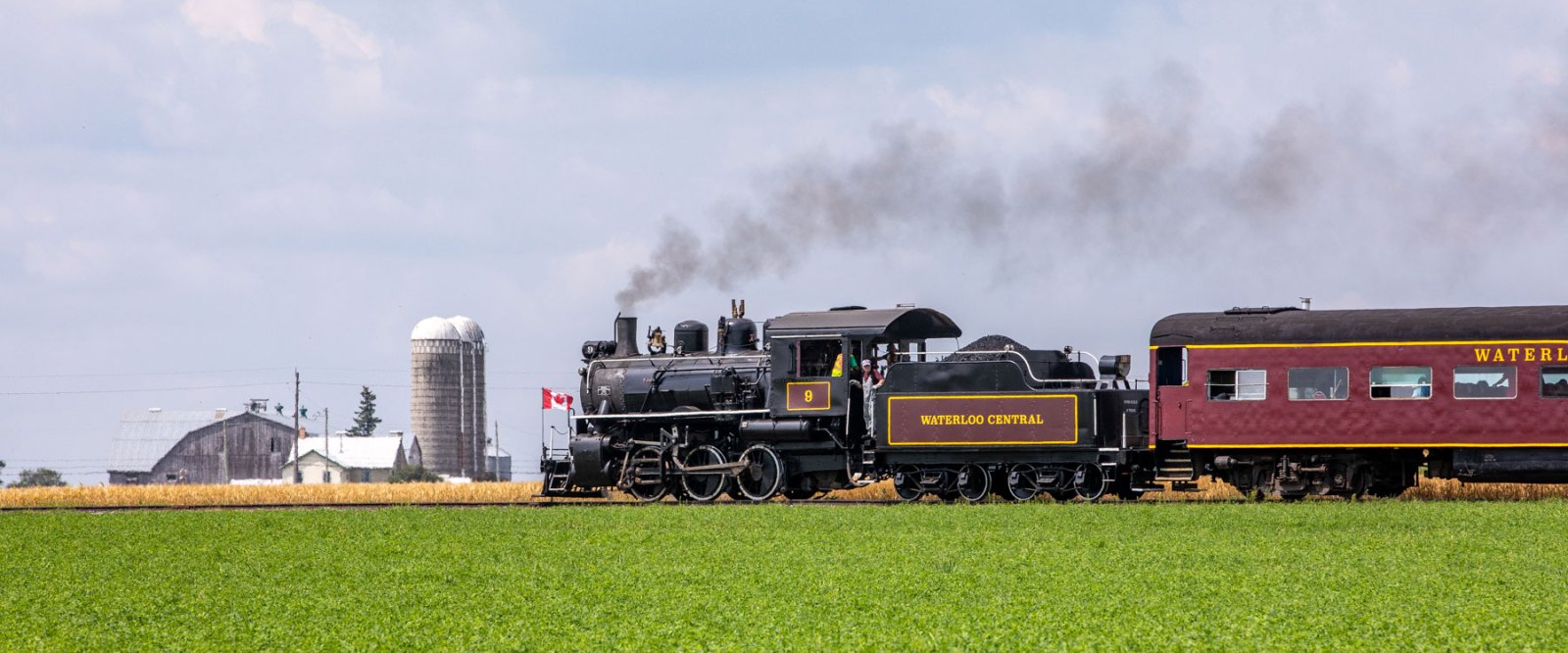 a steam engine train traveling down train tracks near a field