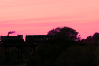 Silhouette of a train on a bridge against a pink sunset sky.