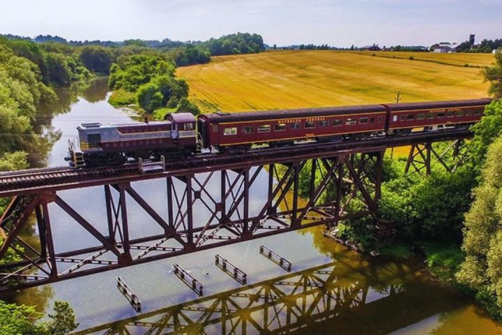 Train crossing a bridge over a river, surrounded by fields and trees.