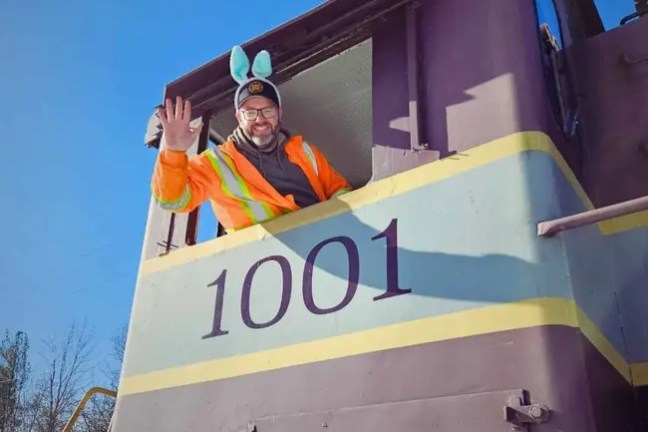 Person with bunny ears waves from train cab labeled '1001.'