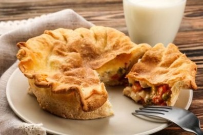 A pie on a plate with a slice cut, next to a fork and a glass of milk on a wooden table.