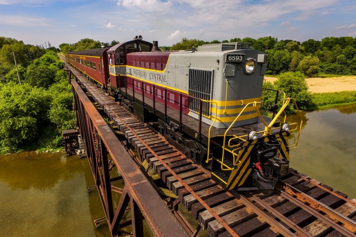 Train on bridge over river in countryside, lush greenery around.