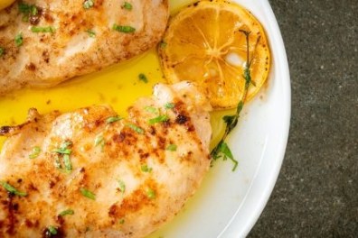 Grilled chicken breasts with lemon slices and herbs on a white plate.