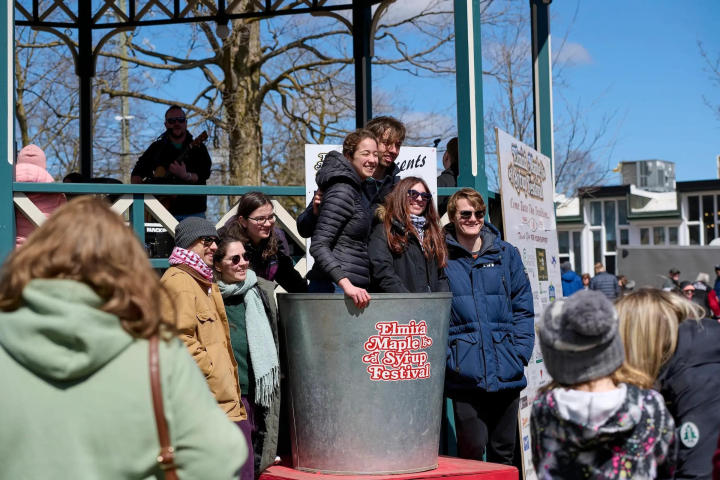 Group of people posing around a large bucket at a festival on a sunny day.