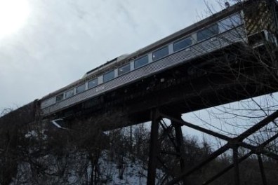 Train crossing a tall bridge over a snowy, wooded area.