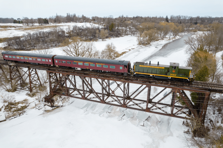 Train crossing a snowy river on a steel trestle bridge in a winter landscape.