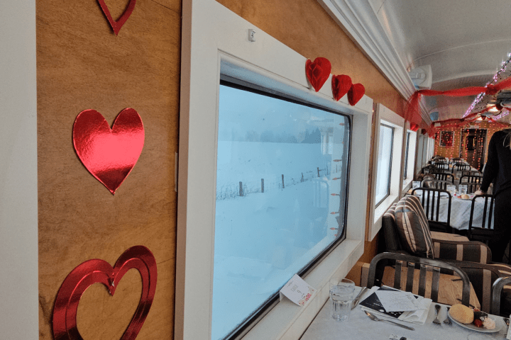 Train dining car with red heart decorations and a snowy window view.