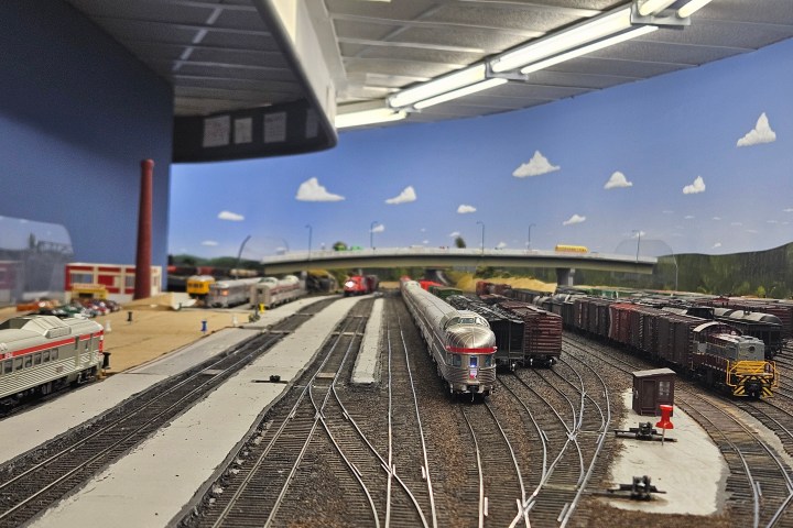 Model train set with tracks, trains, and a backdrop of sky and clouds.