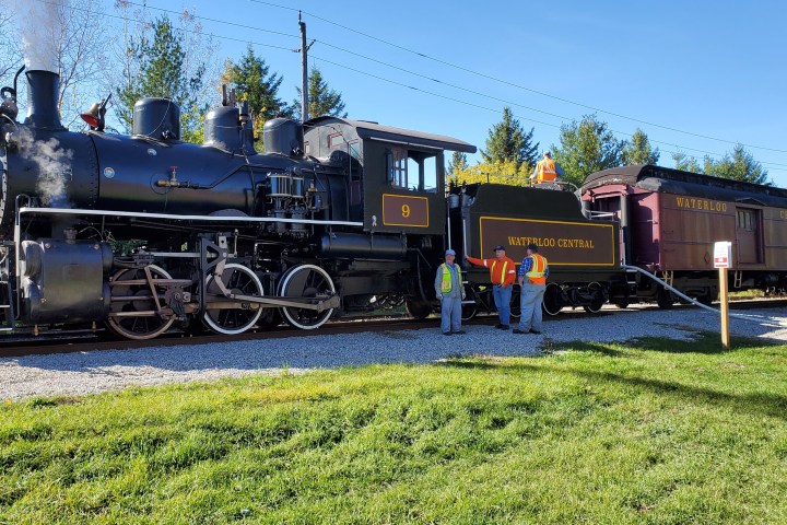 Steam locomotive with 'Waterloo Central' on side, crew standing beside it on a sunny day.