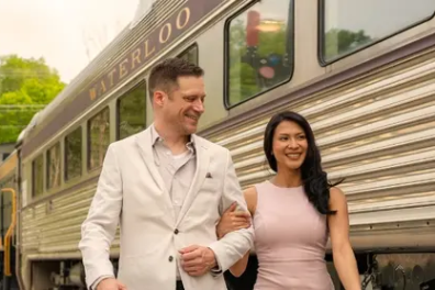 Smiling couple walking beside a vintage train with vibrant food dishes on both sides.