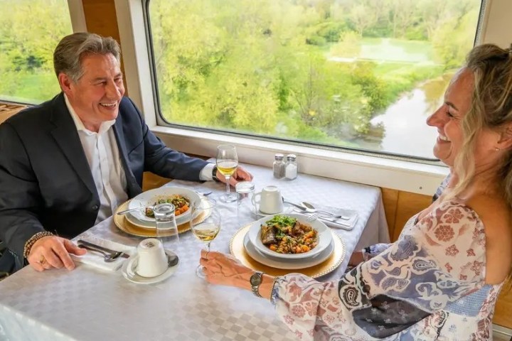 Couple dining on a train with scenic view outside the window.