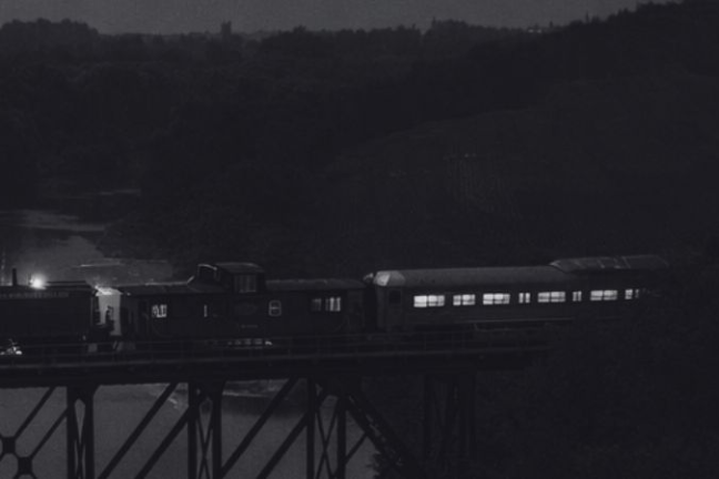 Vintage train crossing bridge at night with four people in 1920s attire in foreground.