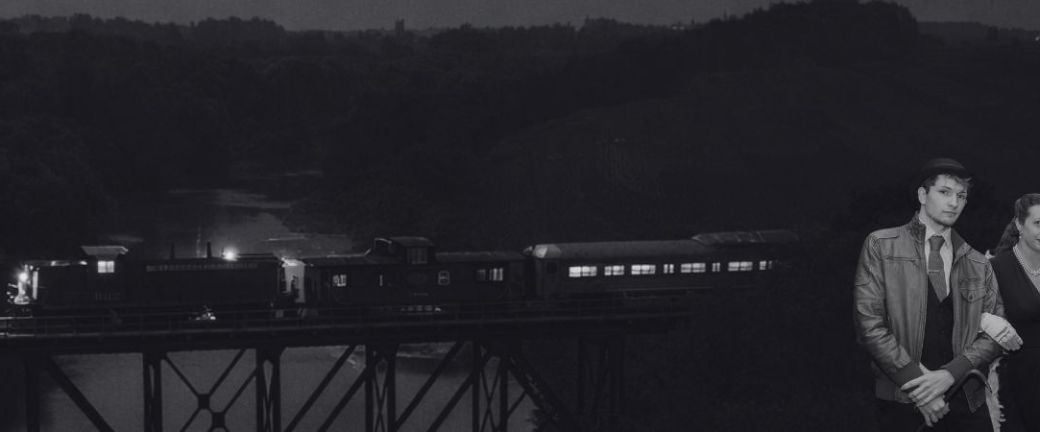 Vintage train crossing bridge at night with four people in 1920s attire in foreground.