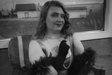 Person in vintage attire sitting with gloves and pearls in a train carriage.