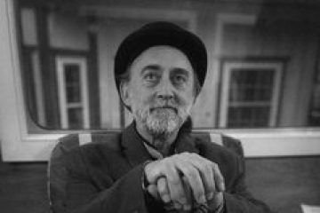 Elderly man with hat and cane sitting indoors, black and white photo.
