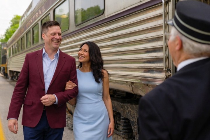Smiling couple walks past a train conductor near a vintage train.
