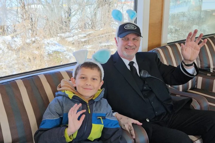 Child and man in bunny ears waving on train seat.