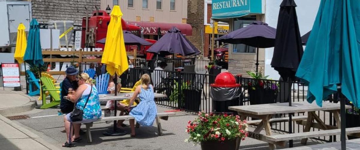 Outdoor dining area with picnic tables and colorful umbrellas, people seated.