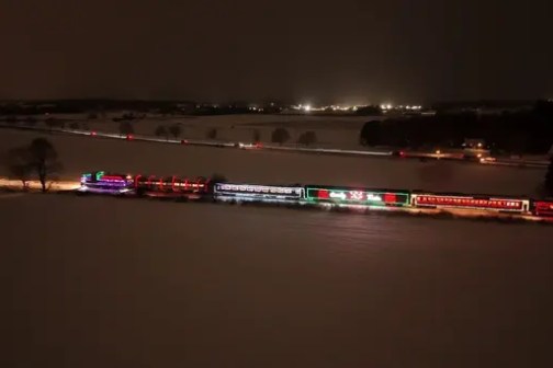 Night scene of a light-decorated train traveling through a snowy landscape.