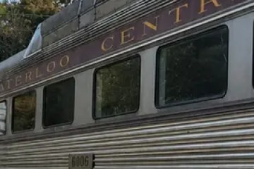Train with ghostly figure waving from window on a sunny day.