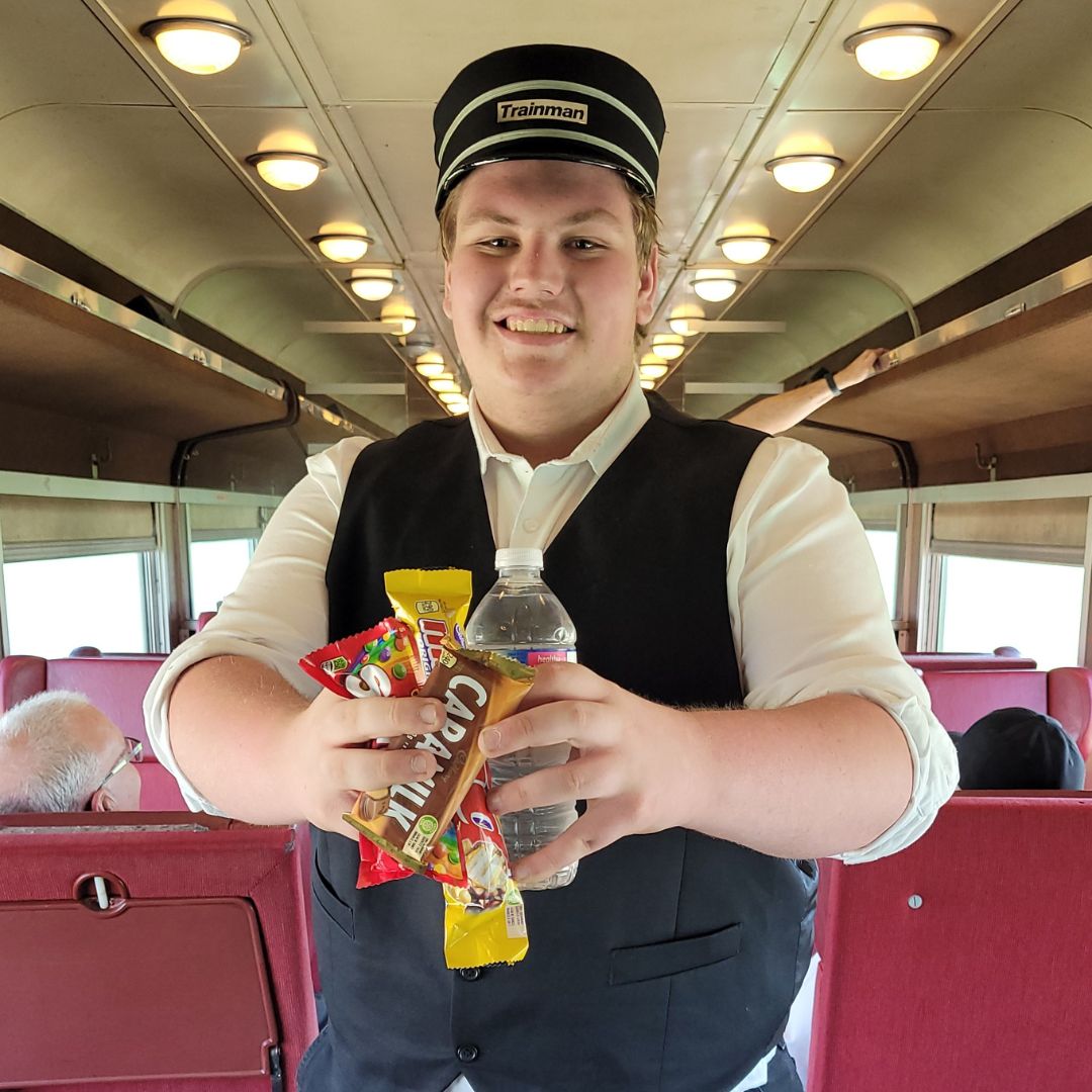 Person in a train uniform holds an assortment of snacks and a drink on a train.