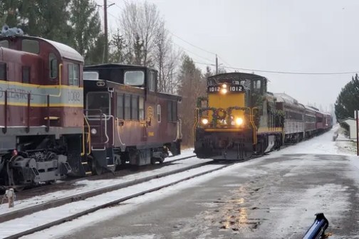 Two trains on snowy tracks, one moving and one stationary.