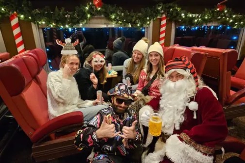Group in festive attire with Santa on a decorated train.