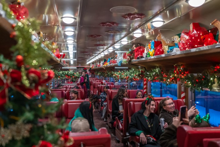 Festive train interior with red seats, Christmas decorations, and passengers taking photos.