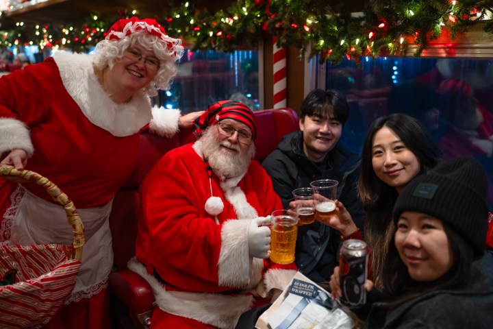 People in festive attire, including Santa, enjoying drinks on a decorated train.