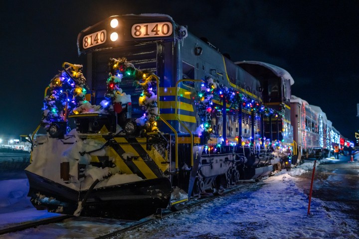 Festive train covered with colorful lights and snow at night.
