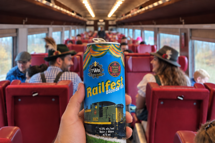 Person holding a beer can inside a train with passengers wearing hats.
